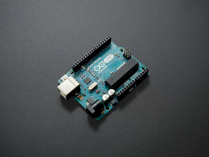Person coding on laptop connected to an Arduino Uno with LEDs and sensors on a workbench